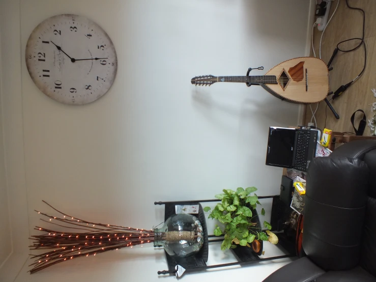 a clock hanging on the wall above a laptop and guitar