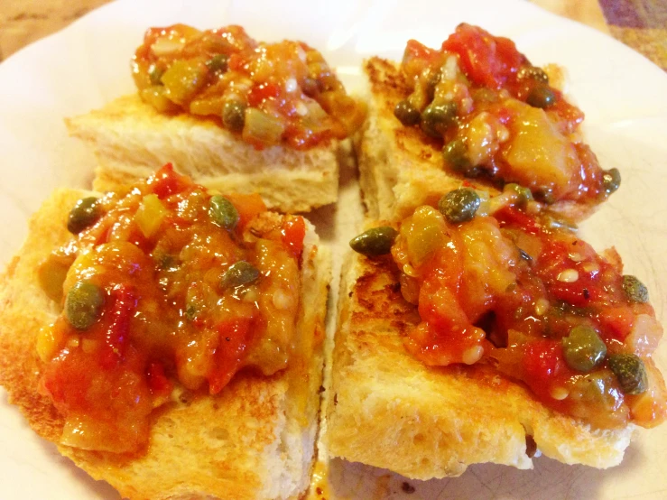 several pieces of sandwich sit on a plate with tomato sauce on top