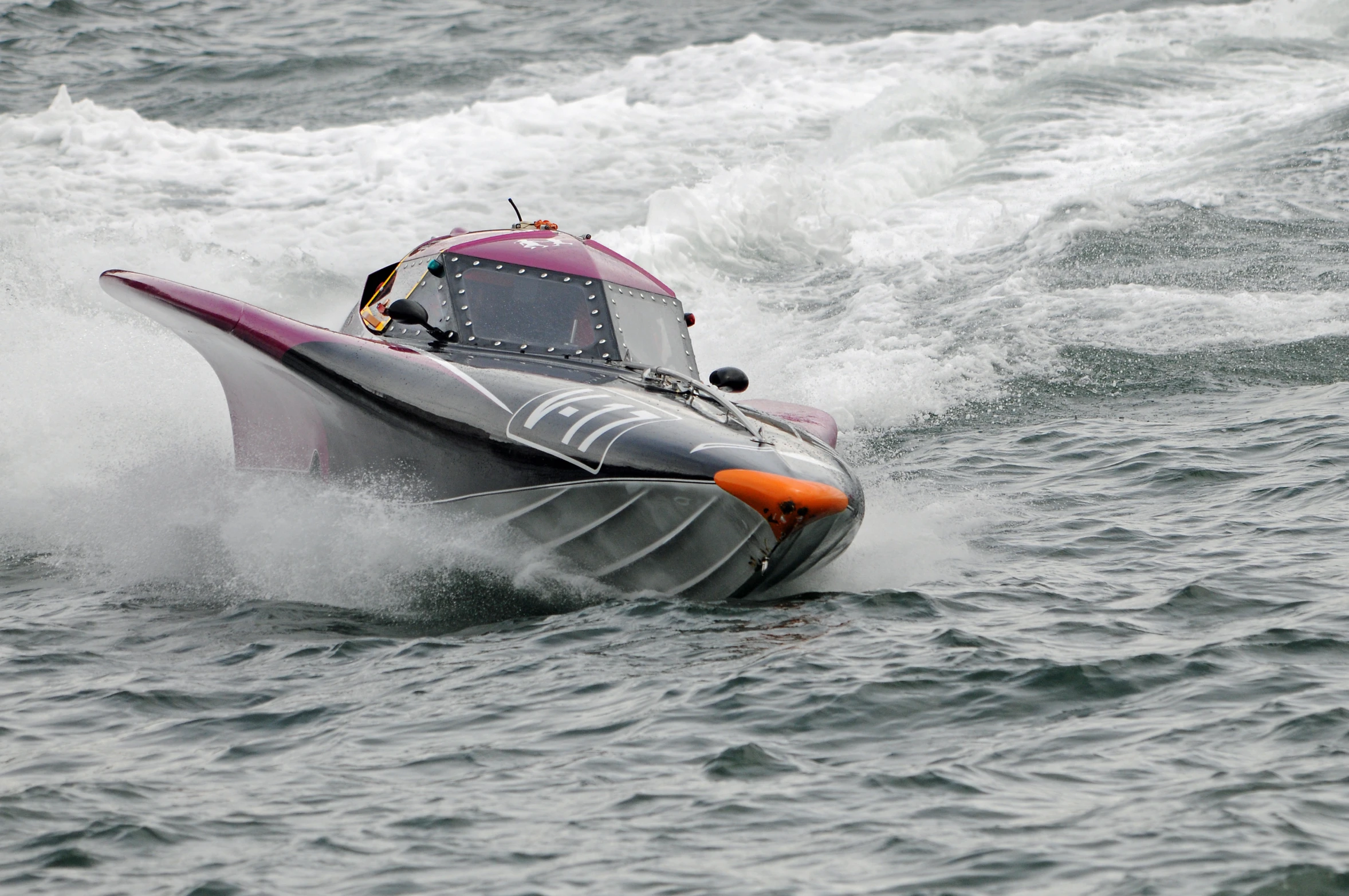 a gray and red boat with an orange top riding through the water