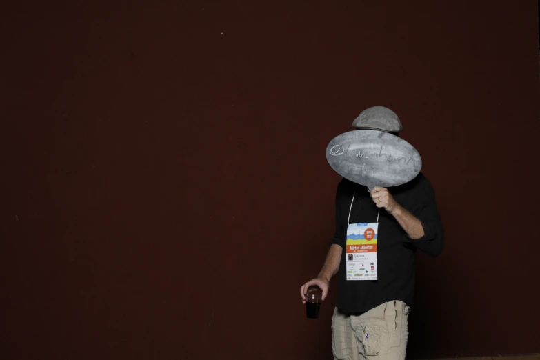 a man holding a soda bottle in his hands and wearing a paper bag hat