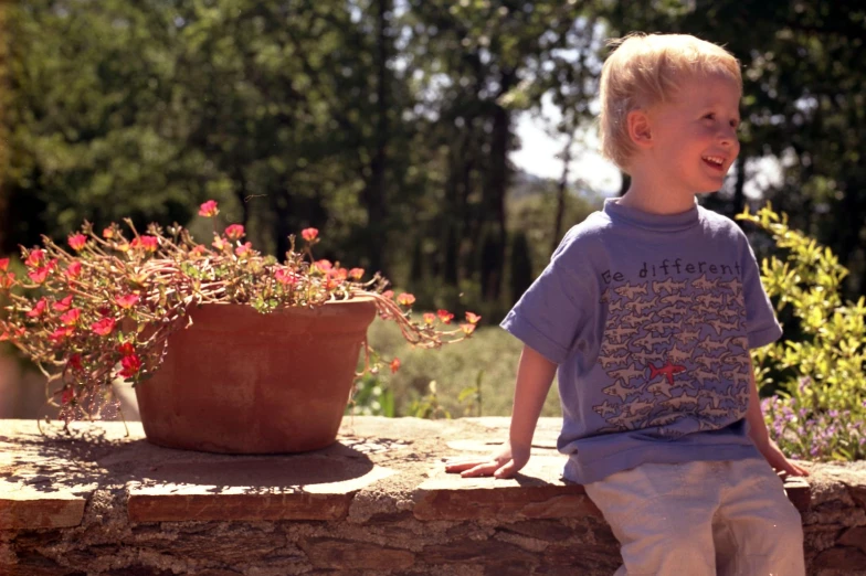 a little boy with blond hair standing by flowers