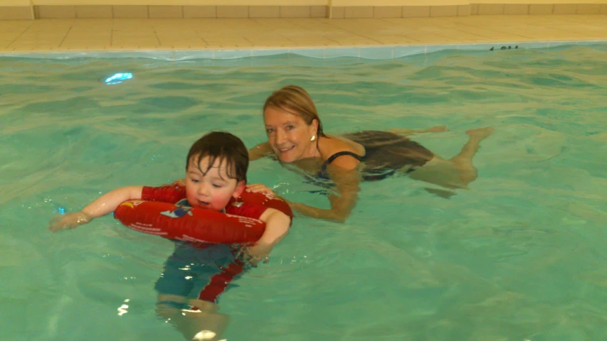 a mom and her son are playing with a toy in the pool