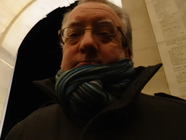 a man wearing a scarf stands in an arch with the archway door open