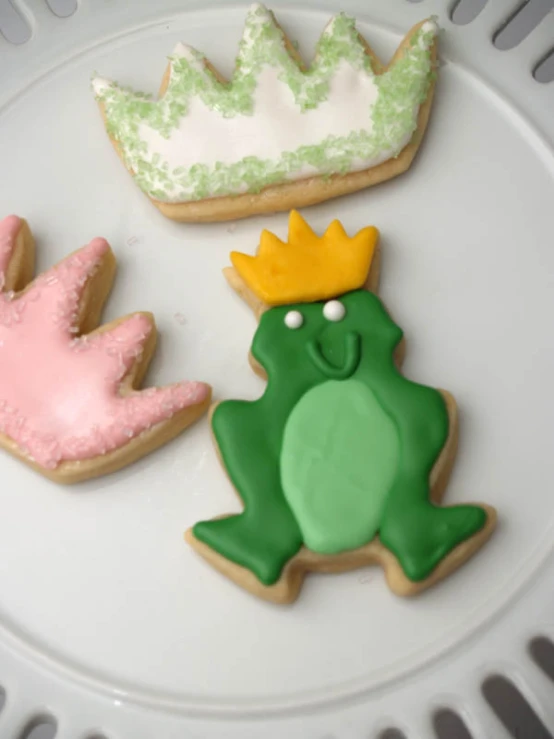 three decorated cookies on a plate with a crown, frog and one bird