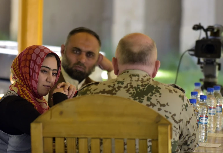 two people sitting at a table talking to a soldier