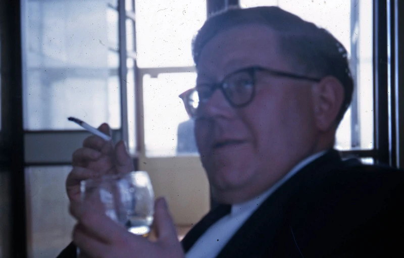 an old man wearing glasses holding a cigarette and a glass