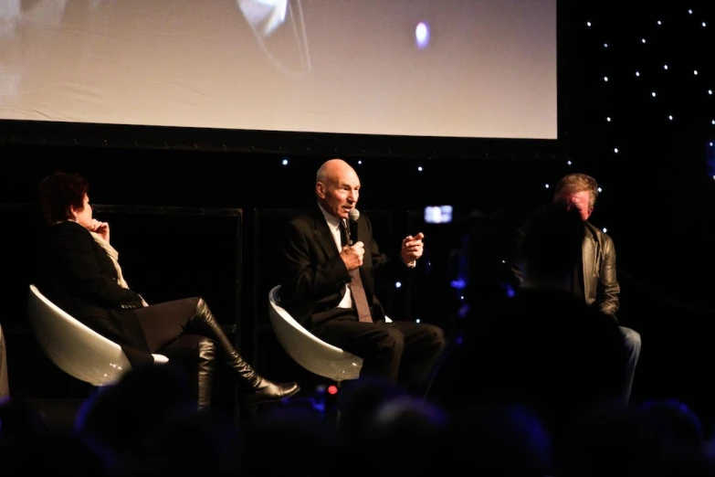 three men in suits are talking on stage