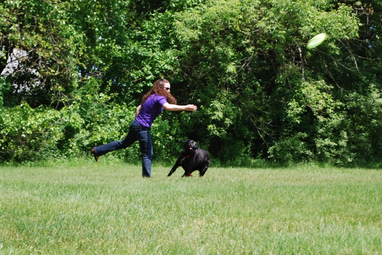 a woman playing frisbee with her dog in a field