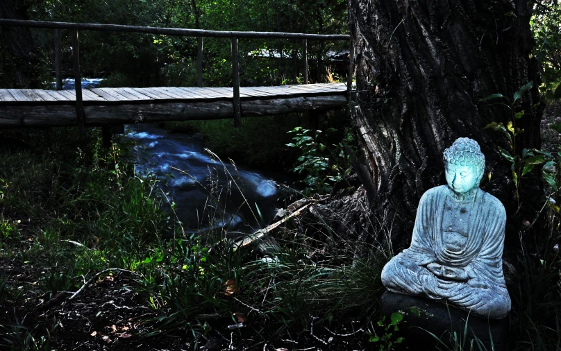 a buddha statue sits next to a stream near a bridge