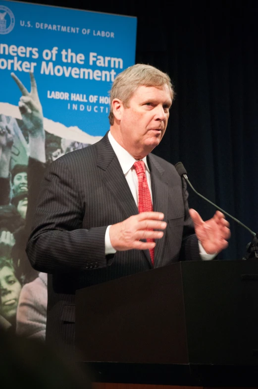 a man in a suit and tie stands at a podium giving a speech