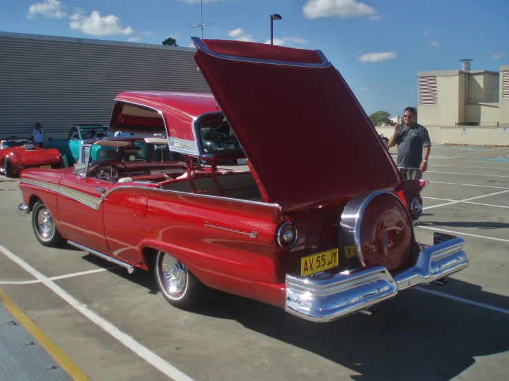 two men stand next to a classic car and have the hood open