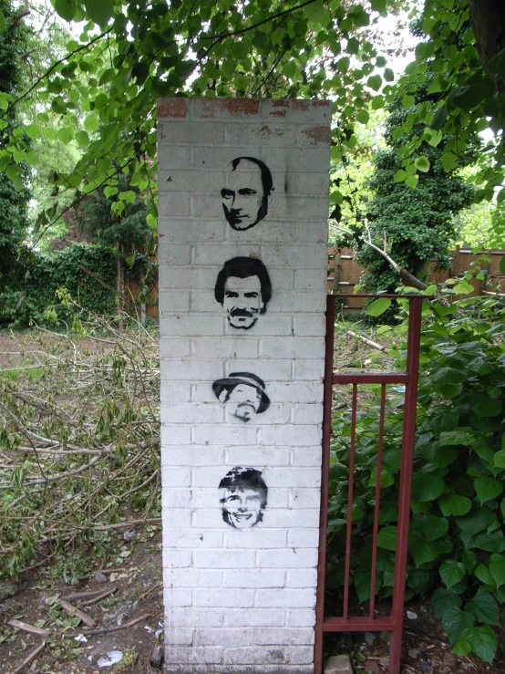 four face graffiti on a brick wall behind a gate