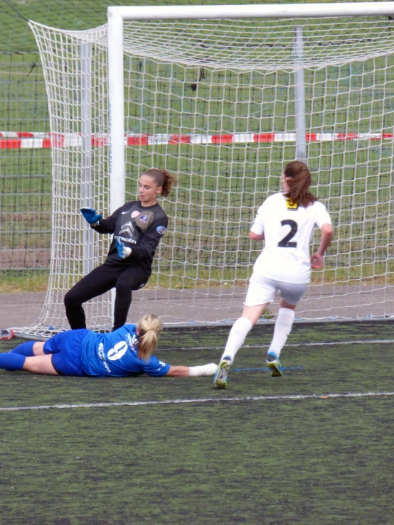 a female soccer player in a blue shirt is in mid air as the girl is lying on the ground behind her