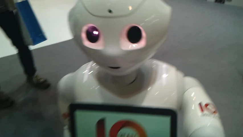 a white robot standing in a room with a laptop