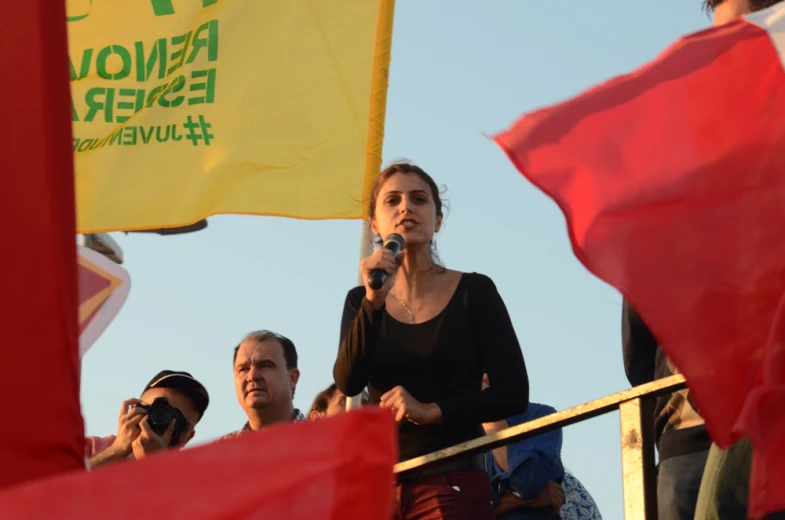 woman speaking into microphone surrounded by people with flags