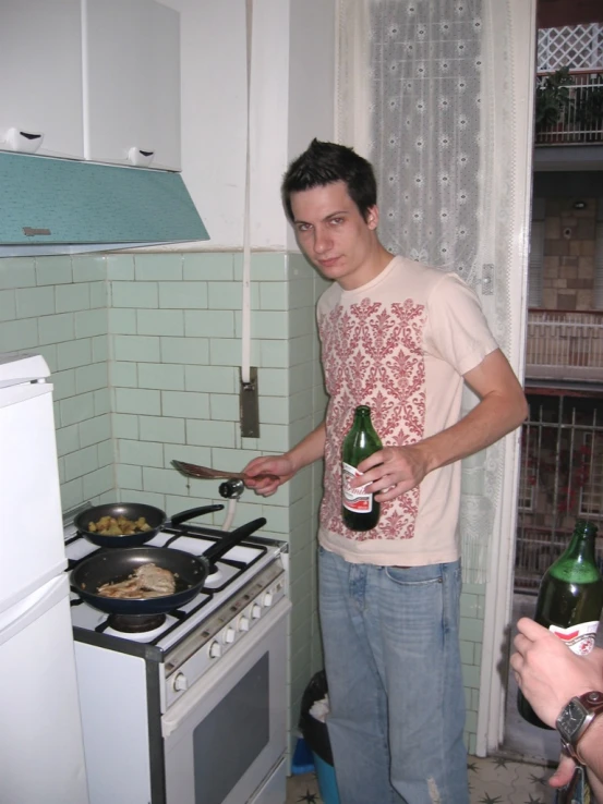a man holding a bottle of beer while standing in front of a stove