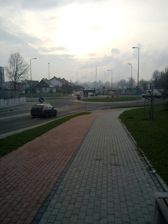 a paved pathway by the road with cars parked on it