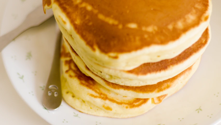 a stack of three pancakes with a knife and fork on a plate