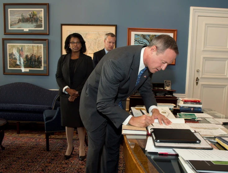 a man wearing a suit bending down with paperwork on a desk