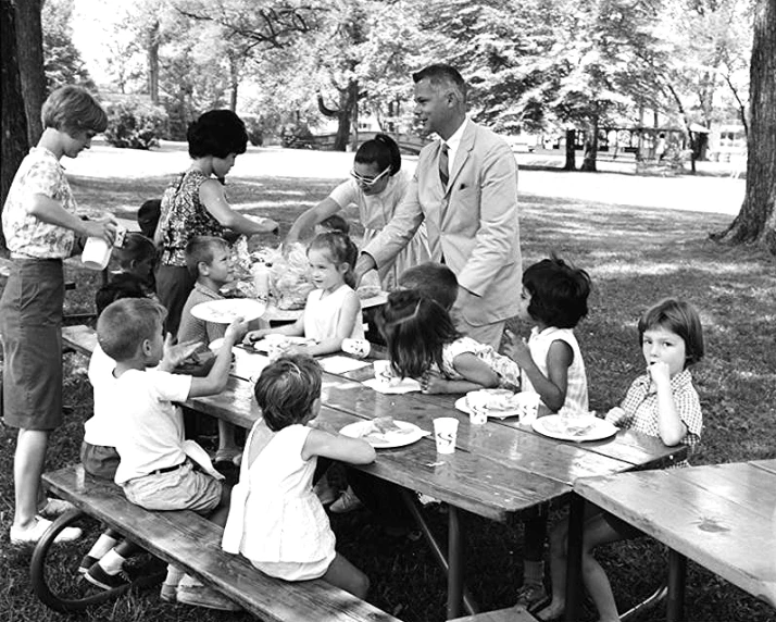 a group of children sit at picnic tables and eat a meal