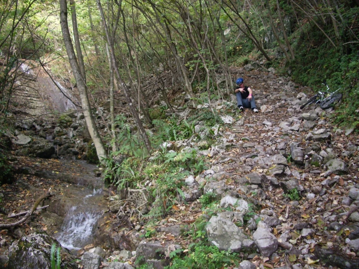 a man with a back pack sits on the side of a stream in the woods