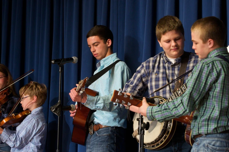 three s playing guitars and guitar in front of a microphone