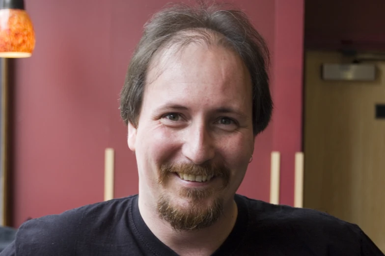 man smiling with dark shirt and red wall in background