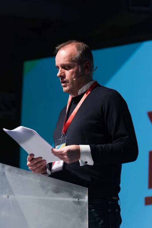 man at podium giving a speech holding a paper