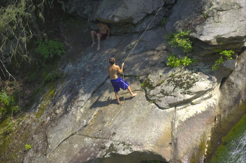a man on a rock climbing up a hill near another guy