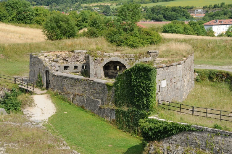 an old building with green roof next to fence and hills