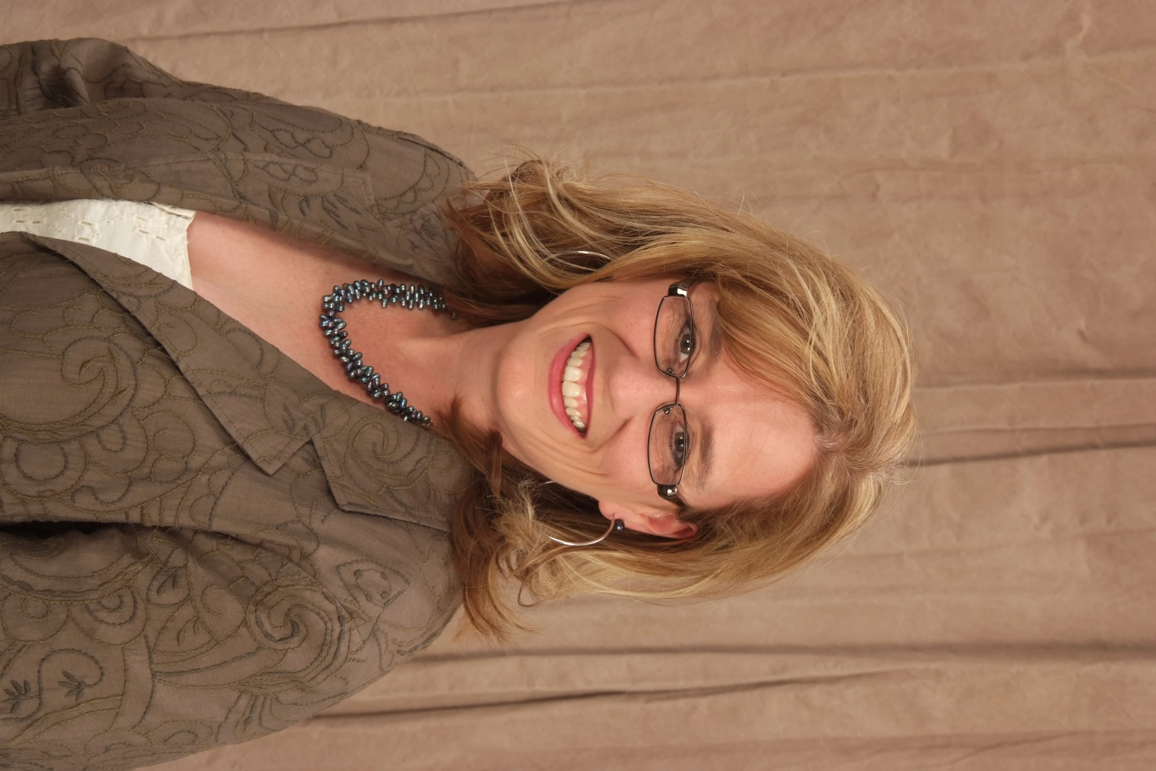 a woman wearing glasses and a brown blazer smiles