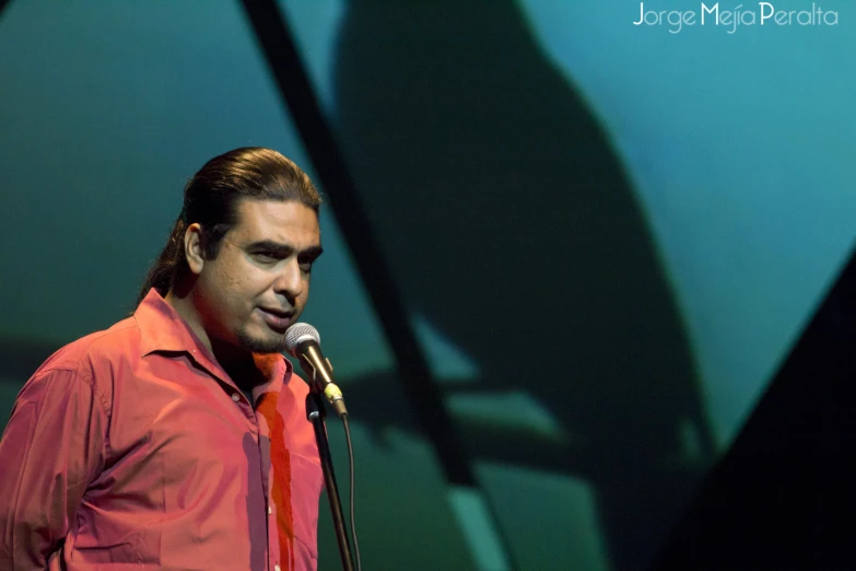 a man in a red shirt standing with a microphone