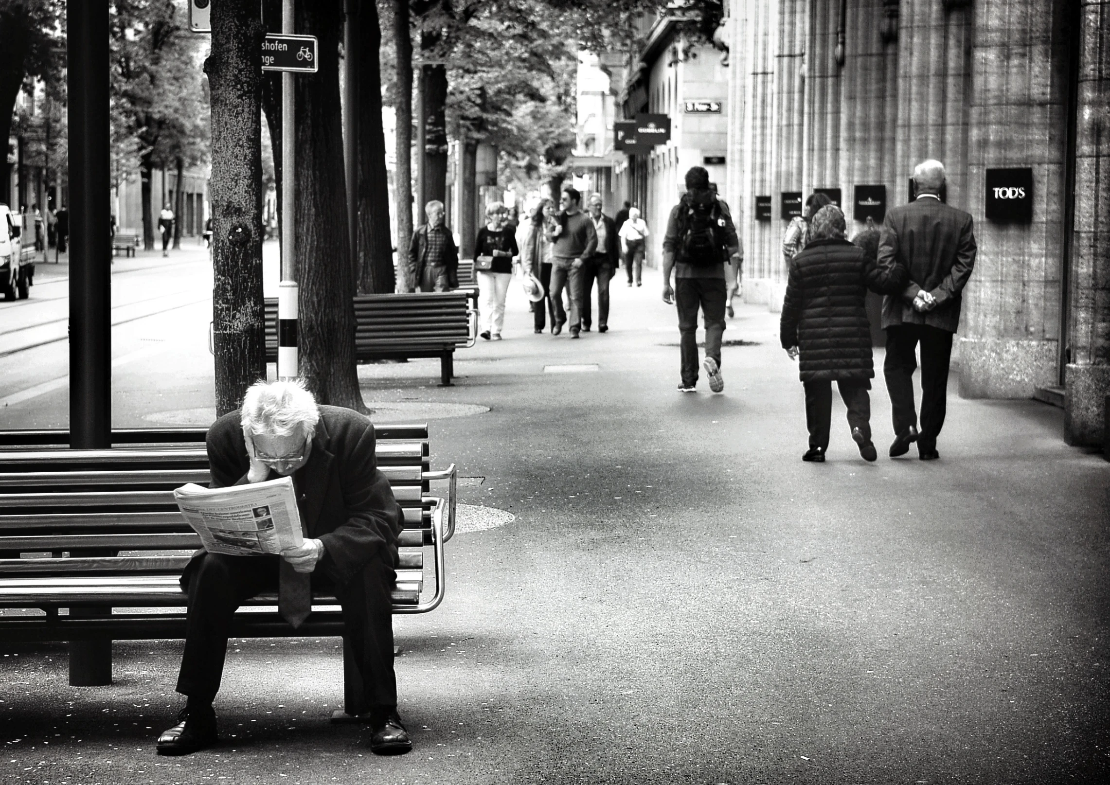 man sitting on bench in middle of street reading paper