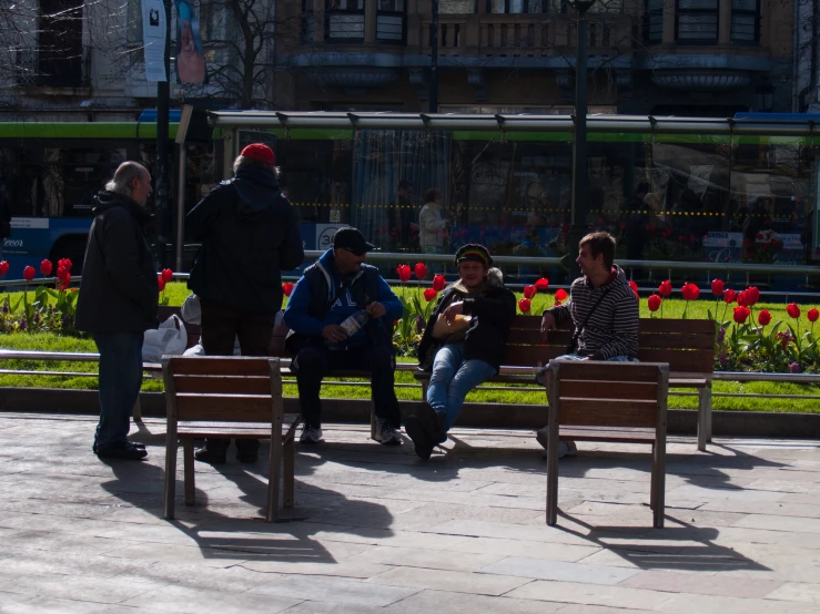 a group of people sitting on a park bench in the shade