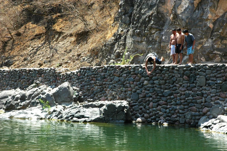 two guys stand on the rocks by water and look at soing