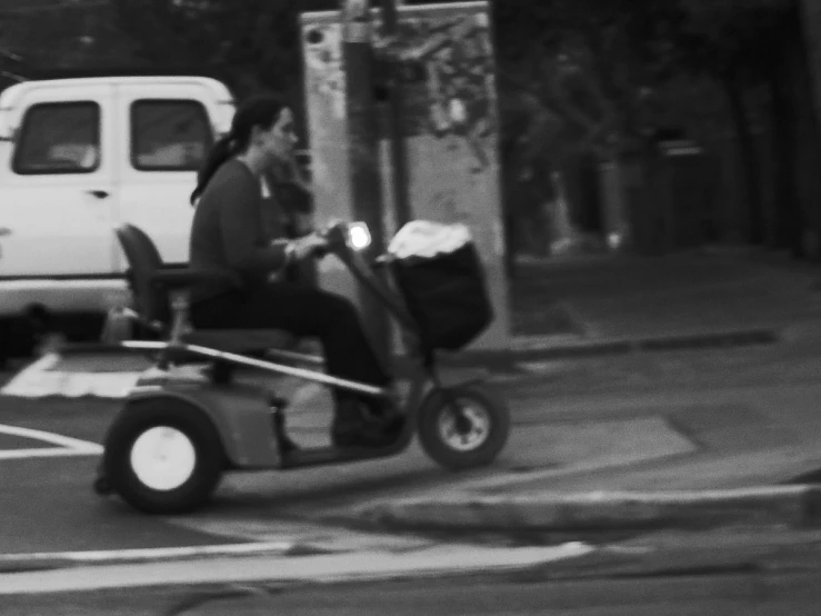 two people sit on a motorized moped across a parking lot