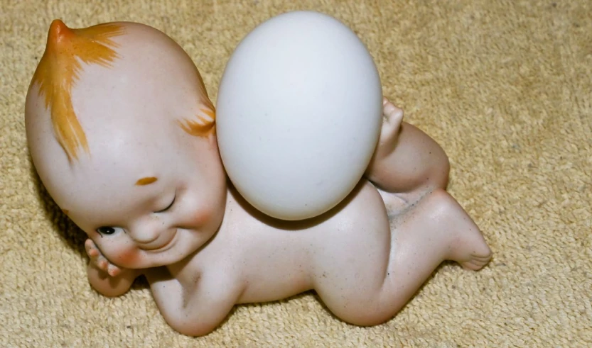 a porcelain baby is sleeping on the floor next to an egg