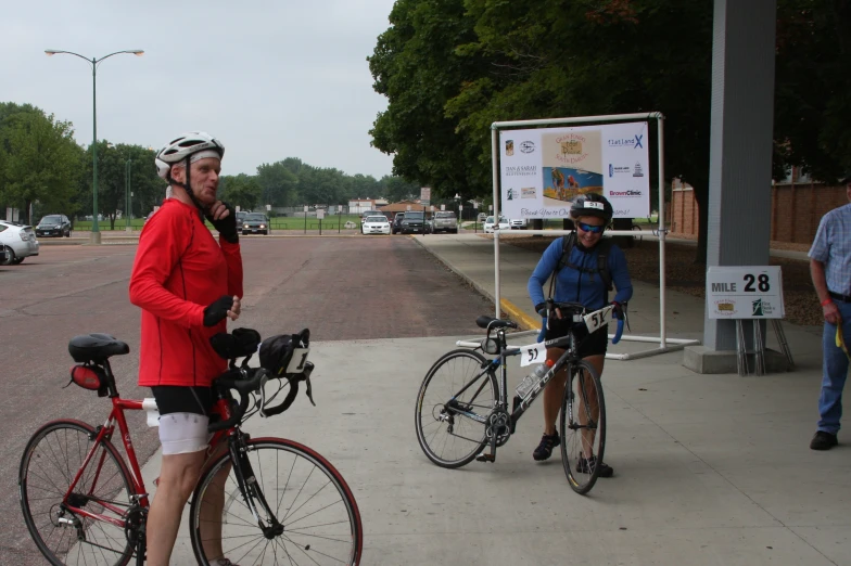 man riding bicycle and woman wearing red jacket in front of poster