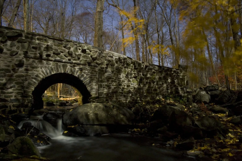 an old stone bridge over a small creek in a wooded area