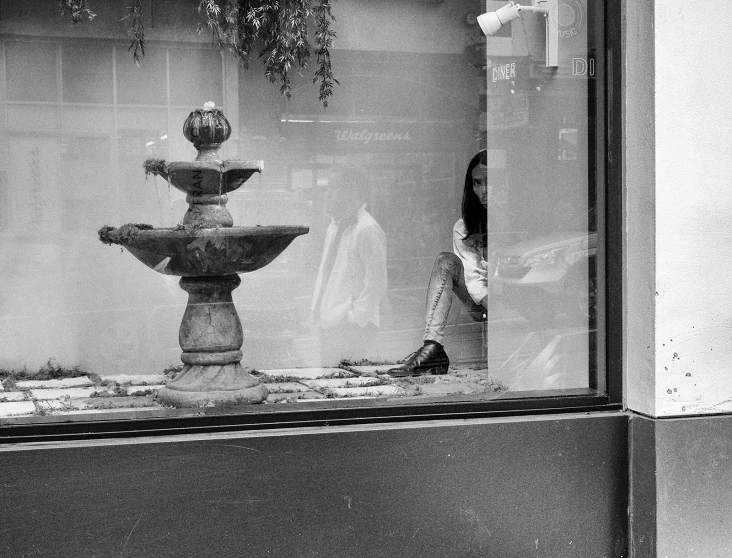 a  walks past a water fountain through a shop window