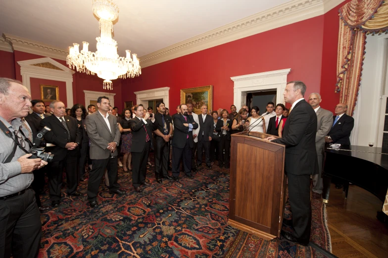 a man talking at a podium surrounded by people