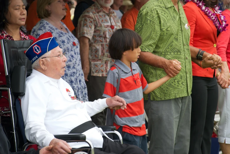 an old man sitting in a wheel chair, surrounded by people