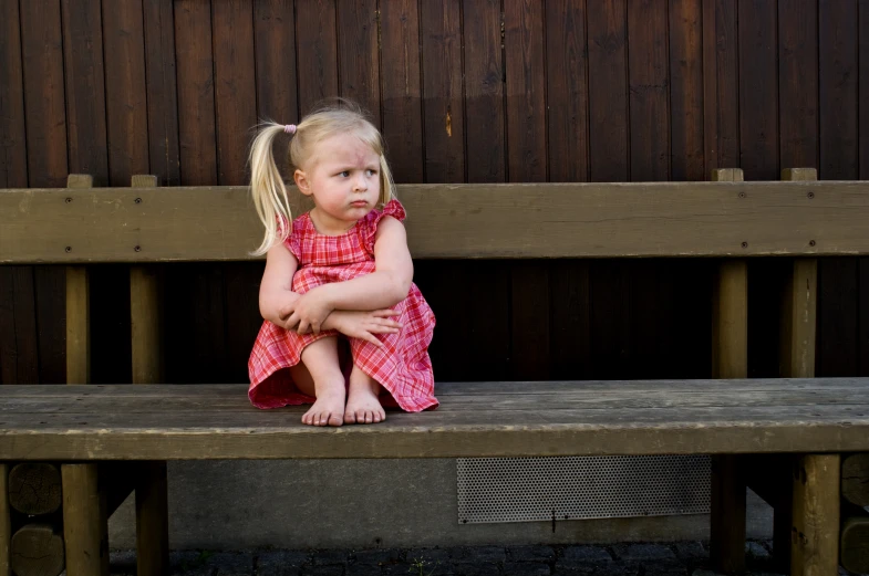 a little girl sitting on top of a wooden bench