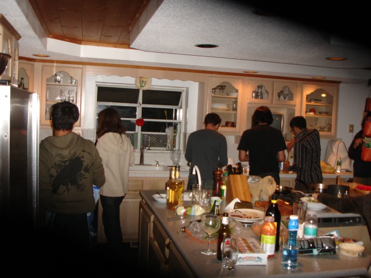 a group of people standing in a kitchen with the refrigerator open