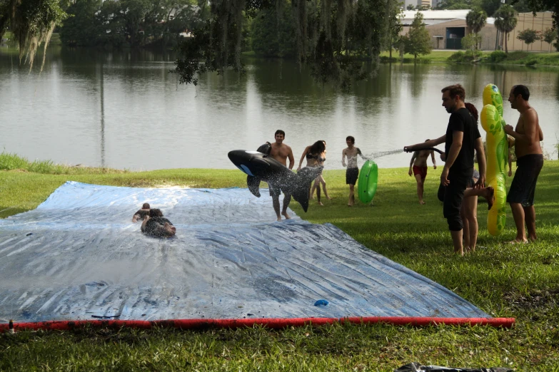 a group of people stand around and watch a man jumping a water slide