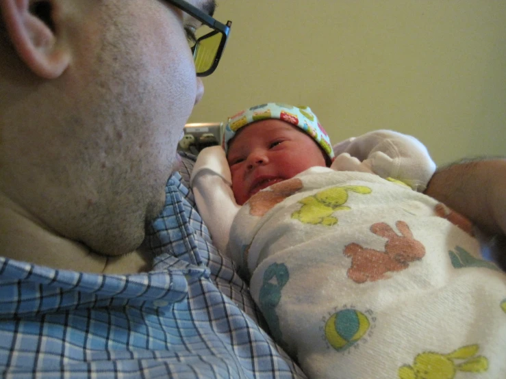 a newborn baby wearing a bib and hat being held up by his father