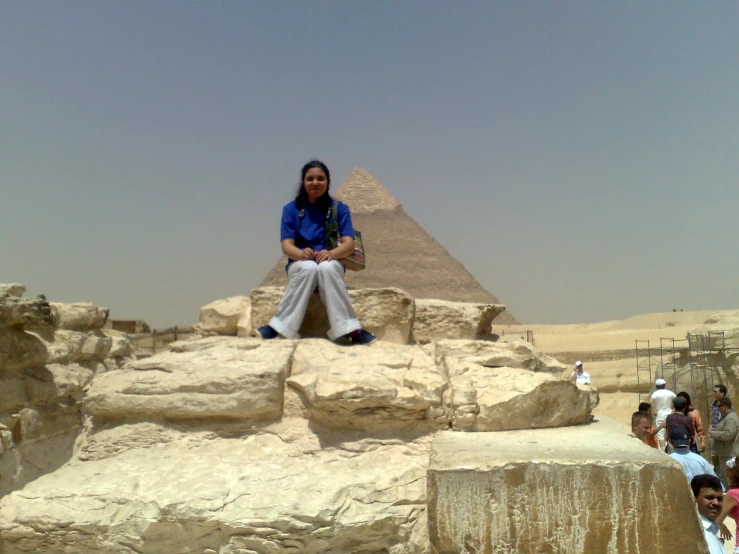a woman sitting on top of some rocks near a pyramid