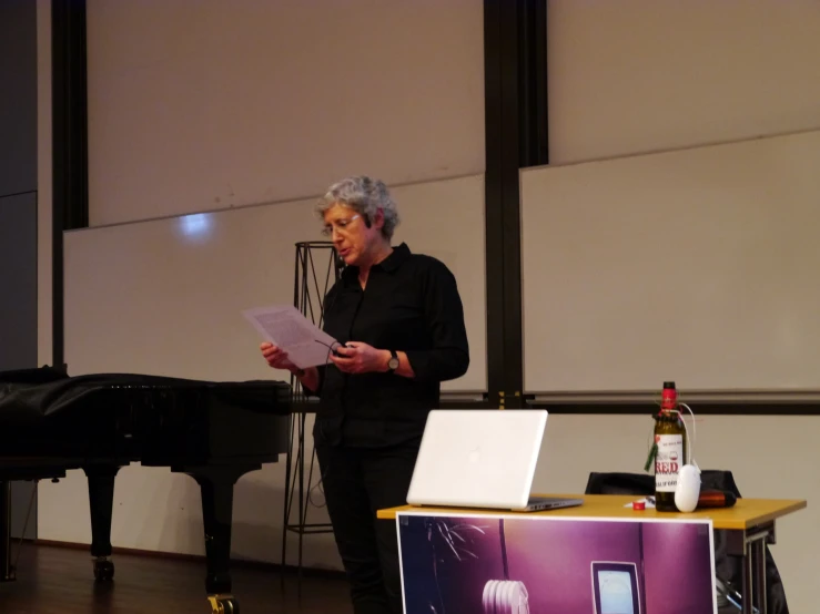 a woman in black jacket standing at a table next to a piano