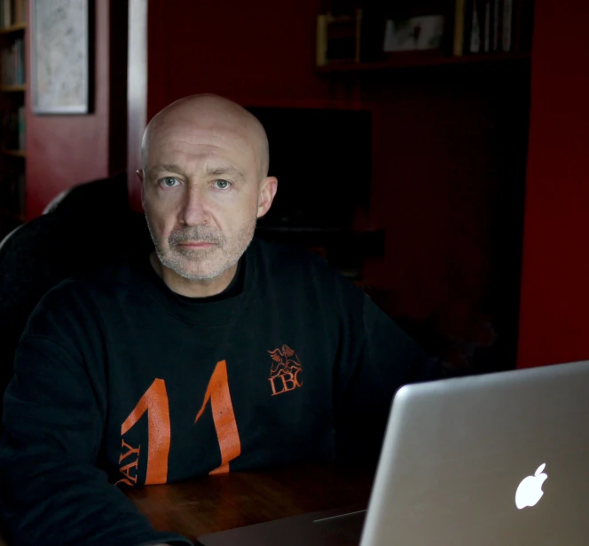 man with bald head and wearing a t - shirt is sitting in front of a computer