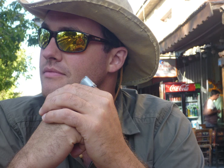 man wearing sun glasses and a hat sitting down with his arm crossed